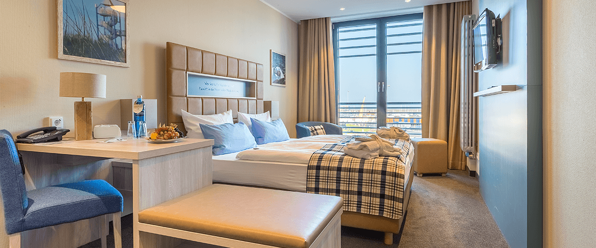 Blick ins Hotelzimmer mit Tisch, Doppelbett und bequemem Sessel