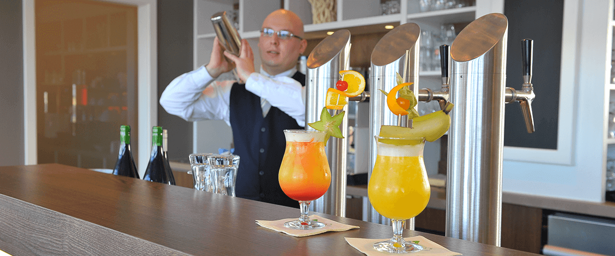 Barkeeper bei der Herstellung köstlicher Cocktails, sowie bereits zwei fertige Cocktails auf der Theke