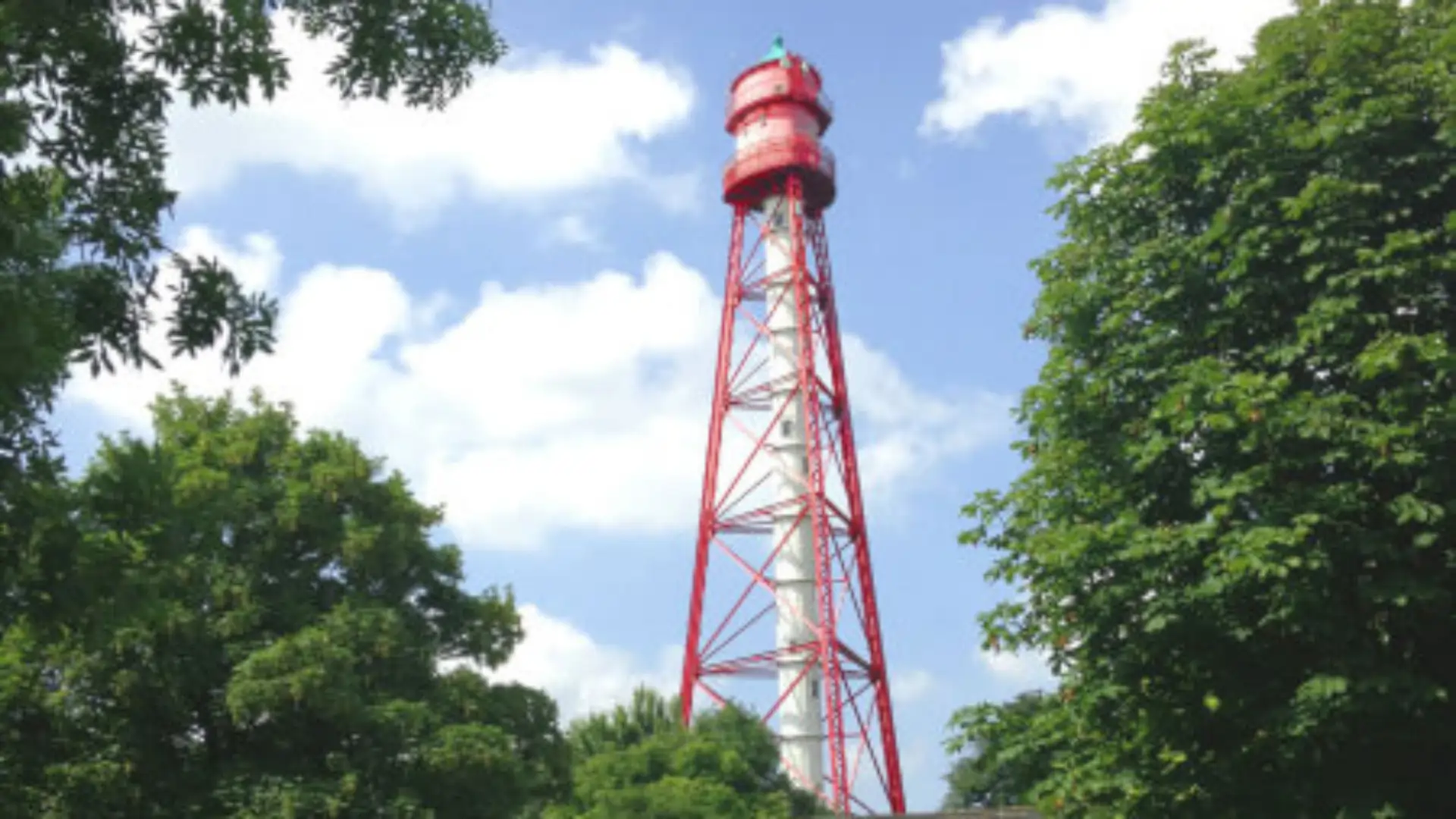 Blick auf den Campener Leuchtturm umrahmt von grünen Bäumen